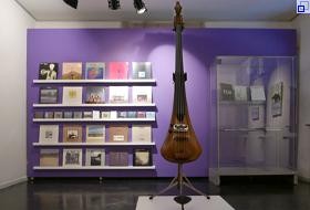 Ein Raum der Ausstellung "Eberhard Weber". An der Wand ein Regal, auf dem Schallplattenhüllen stehen, in der Mitte des Raumes ist der elektrische Bass von Eberhard Weber ausgestellt.