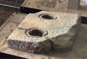 Beschädigter Stein mit zwei runden Löchern.