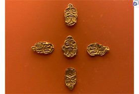 Fünf goldene Plättchen in Form eines Gesichts liegen kreuzförmig auf dem Hintergrund.
