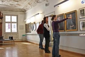 Zwei Besucherinnen und ein Besucher betrachten und diskutieren Porträtgemälde im Patrizierzimmer des Stadtmuseums im Gelben Haus.