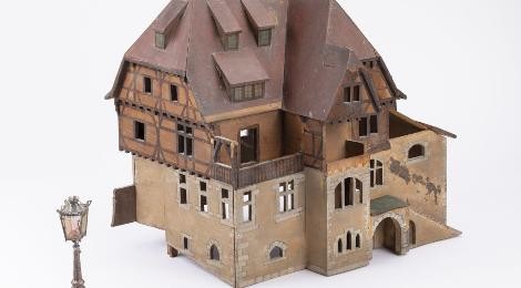 Modell eines Hauses mit Fachwerk und Steinfundamenten. Im Vordergrund steht eine Laterne.