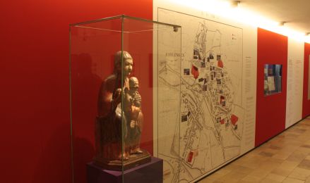 Ausstellungsbereich: Eine Vitrine mit einer gefassten Holzfigur, daneben eine große Übersichtskarte.