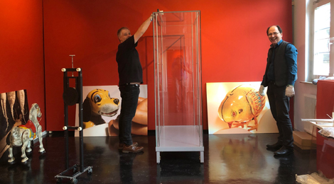Aufbau der Ausstellung Mechanische Tierwelt: Bilder stehen an die Wand gelehnt, 2 Männer arbeiten lachend